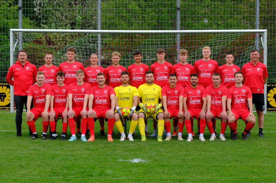 Fußballmannschaft in roten Trikots steht vor einem Tor, umringt von Grünflächen.