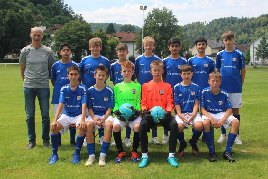 Jugendfußballmannschaft in blauen Trikots, sitzend und stehend auf dem Spielfeld.