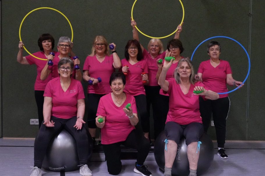 Gruppierung von Frauen in pinken Shirts mit Fitnessgeräten und Reifen.
